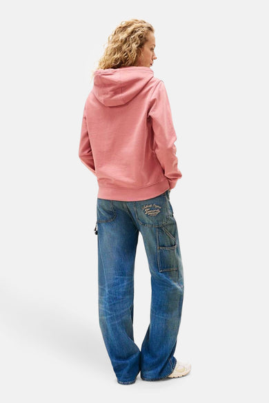 Pull-over rose avec capuche de TOMMY JEANS, associé à des jeans bleus décontractés et des chaussures blanches.