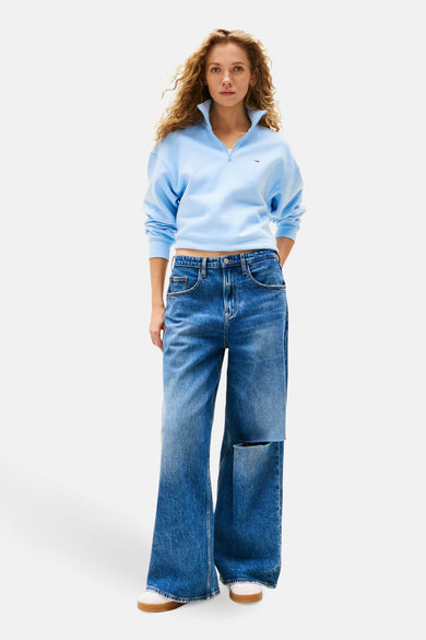 Blauwe sweater van TOMMY JEANS, met een korte rits en gedragen met wijde jeans met scheuren.
