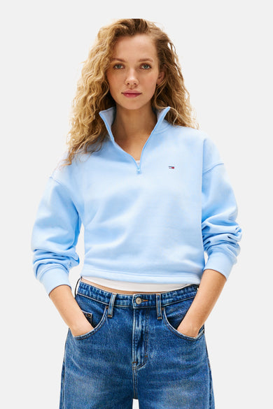 Blauwe sweater van TOMMY JEANS, met korte ritssluiting, gedragen met een blauwe jeans met wijde pijpen.
