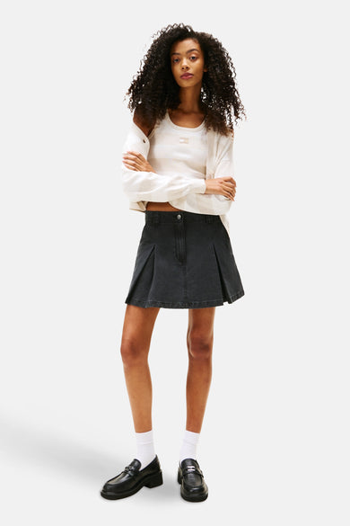Zwarte korte rok van TOMMY JEANS, gecombineerd met een gestreepte top en zwarte loafers met witte sokken.
