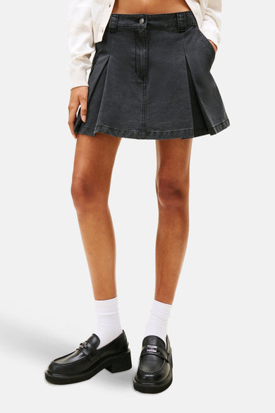 Zwarte korte rok van TOMMY JEANS, geplooide stijl, gecombineerd met witte sokken en zwarte loafers.