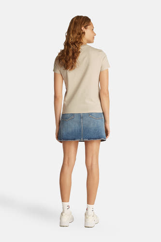 Ecru T-shirt met korte mouwen van TOMMY JEANS, met een spijkerrok en witte sportschoenen.
