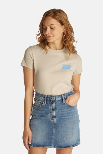 T-shirt écru à manches courtes de TOMMY JEANS, associé à une jupe en denim et à des baskets blanches.