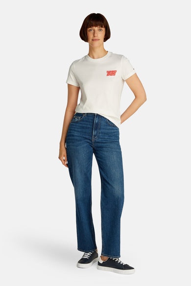 Wit T-shirt met korte mouwen van TOMMY JEANS, met rode tekst op de borst, gecombineerd met blauwe jeans en zwarte sneakers.
