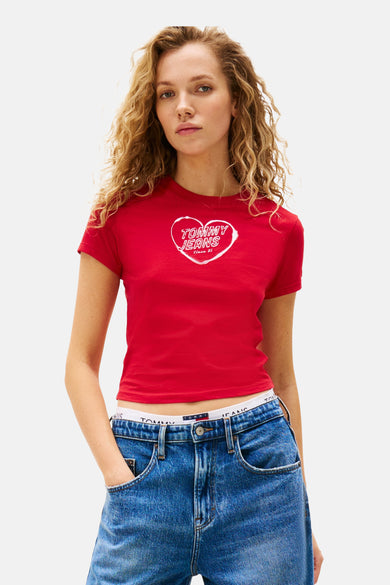 Rood T-shirt met korte mouwen van TOMMY JEANS, met een wit hartlogo op de borst, gecombineerd met een blauwe jeans.
