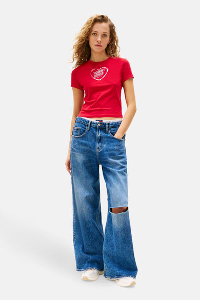 Rood T-shirt met korte mouwen van TOMMY JEANS, met hartvormige print, gecombineerd met wijde jeans met een gat bij de knie.
