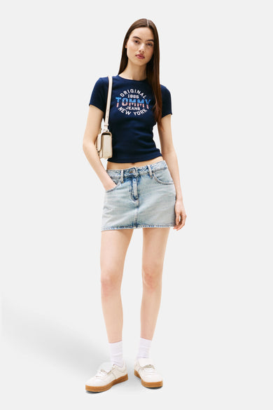 T-shirt bleu marine à manches courtes de TOMMY JEANS, avec impression et associé à une jupe en denim.