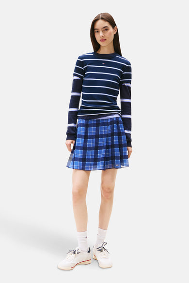 Robe bleue courte de TOMMY JEANS, avec un motif à carreaux et associée à une chemise rayée, des chaussettes blanches et des baskets.