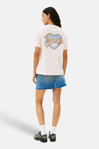 T-shirt blanc à manches courtes de Tommy Jeans, avec un logo retro Tommy sur le dos, associé à une jupe en denim et des baskets.