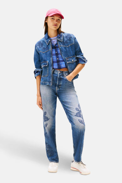 Jeansjas van blauw denim van TOMMY JEANS, met bloemmotieven en gecombineerd met een geruite blouse en roze pet.