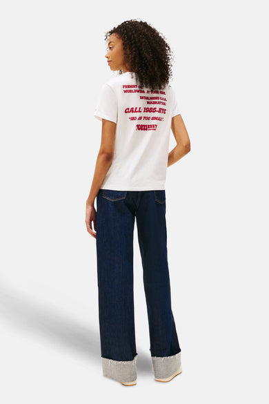 T-shirt blanc à manches courtes de Tommy Jeans, avec imprimé texte rouge sur le dos, porté avec des jeans larges.