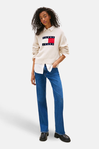 T-shirt écru Tommy Jeans avec col rond, doté d'un design de logo sur la poitrine, associé à une chemise blanche et des jeans bleus.