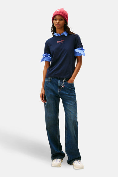 T-shirt bleu à manches courtes de TOMMY JEANS, porté avec un chemisier en dessous et une beanie rose.