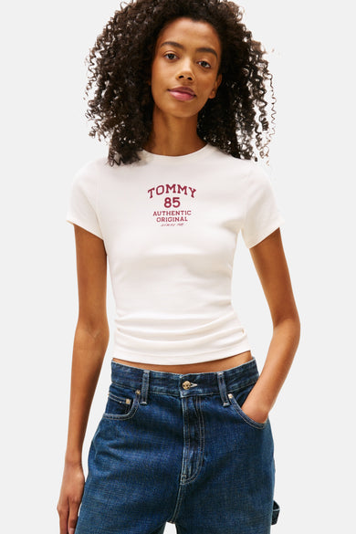 T-shirt blanc à manches courtes de TOMMY JEANS, avec du texte rouge, associé à des jeans bleus et un chemisier à carreaux autour de la taille.