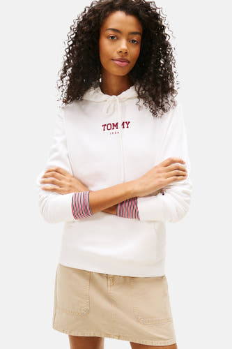 Pull-over blanc à capuche de TOMMY JEANS, avec des manches rayées et associé à une jupe beige, des chaussettes blanches et des baskets crème.