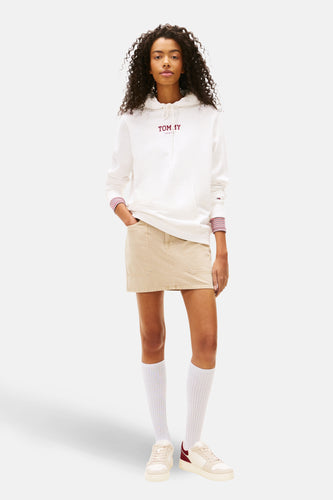 Witte sweater met kap van TOMMY JEANS, met gestreepte manchetten en gecombineerd met een beige rok, witte sokken en crèmekleurige sneakers.