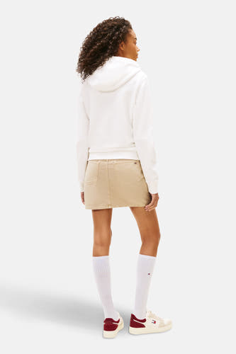 Pull-over blanc avec capuche de Tommy Jeans, vu de derrière, avec une jupe beige, des chaussettes blanches et des chaussures basses.