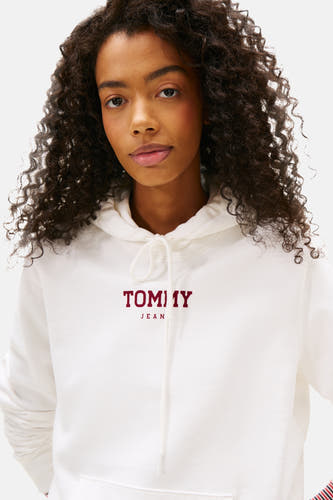 Pull-over blanc à capuche de Tommy Jeans, avec le nom de marque rouge sur l'avant, vu de face.
