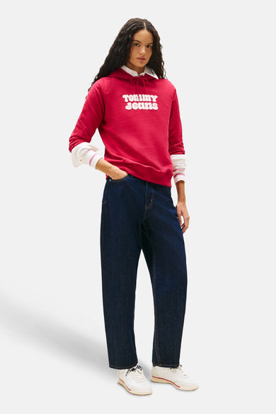 Pull-over rose de TOMMY JEANS avec un col blanc, associé à des jeans noirs et des baskets blanches.