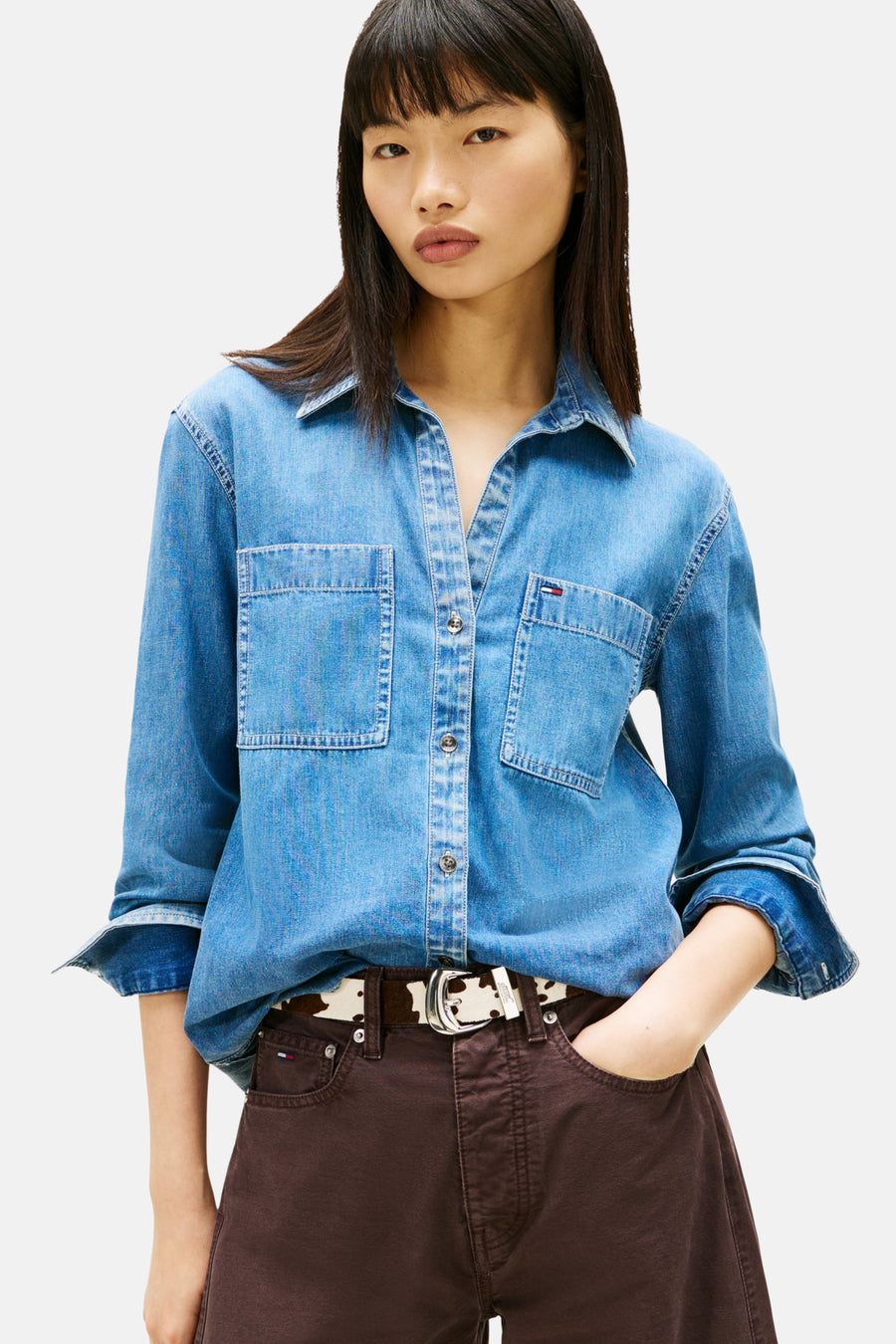 Vrouw in een denim overhemd en bruine broek met een koeienprint riem.