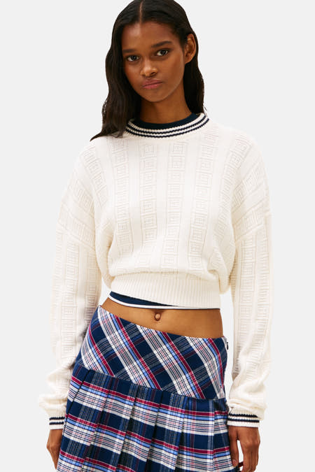 Witte trui met ronde hals van Tommy Jeans, met geometrisch jacquardpatroon en geribbelde boorden, gecombineerd met geruite minirok.
