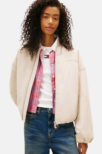Manteau court beige de TOMMY JEANS, avec des manches longues et porté sur des jeans larges.