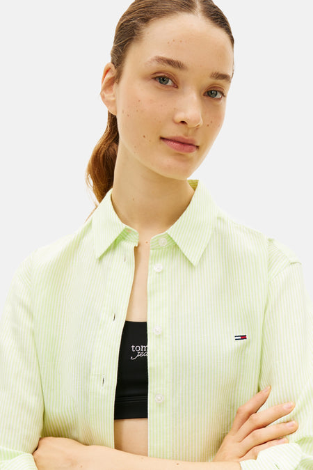 Groen-wit gestreept hemd met lange mouwen van TOMMY JEANS, oversized, met subtiel logo en gedragen over een zwarte sporttop.