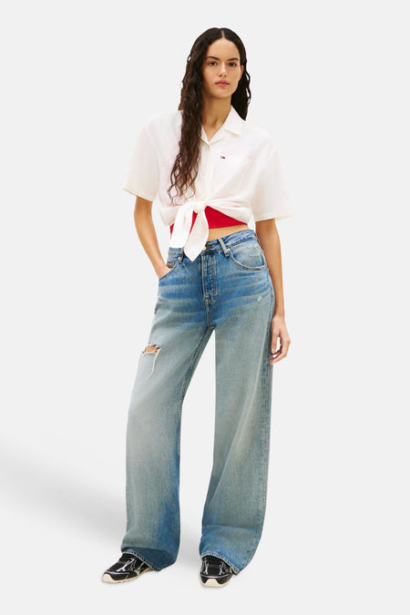 Wit hemd met korte mouwen van TOMMY JEANS, geknoopt met een rode top en blauwe jeans.