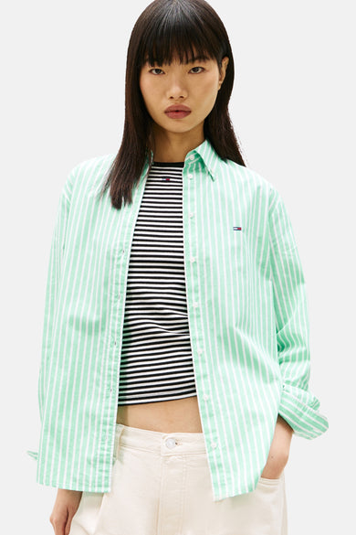 Groen hemd met lange mouwen van TOMMY JEANS, met witte strepen, gedragen over een gestreepte top en een crèmekleurige broek.
