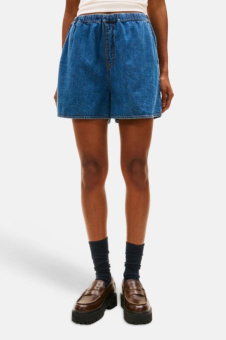 Short en jean bleu moyen de TOMMY JEANS, avec taille élastique, porté avec un t-shirt blanc et une casquette rouge.
