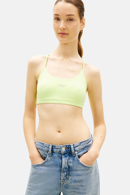 Kort groen T-shirt van TOMMY JEANS met dunne bandjes en merklogo, gedragen met lichte spijkerbroek.
