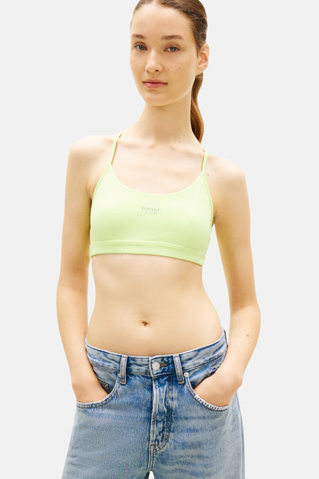 Kort groen T-shirt van TOMMY JEANS met dunne bandjes en merklogo, gedragen met lichte spijkerbroek.