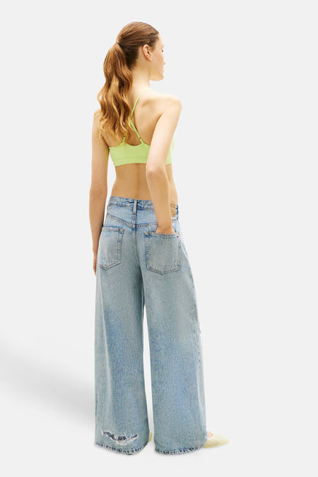 Groen T-shirt van TOMMY JEANS met dunne bandjes, rug van model, gedragen met wijde jeans en gele instappers.