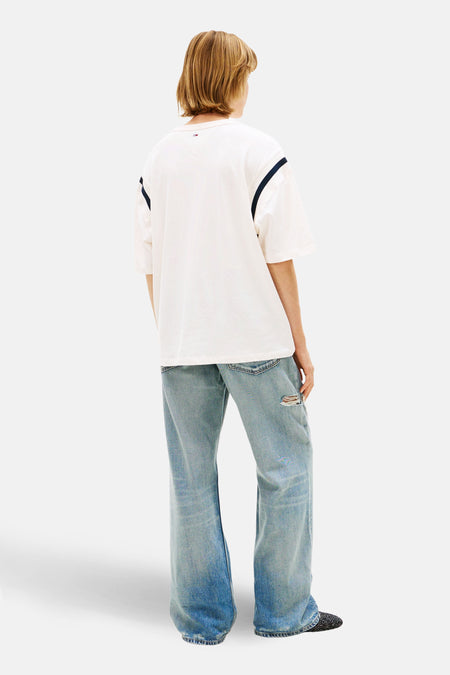 Wit T-shirt met korte mouwen van TOMMY JEANS, met donkerblauwe strepen op de schouders, gedragen met wijde jeans.