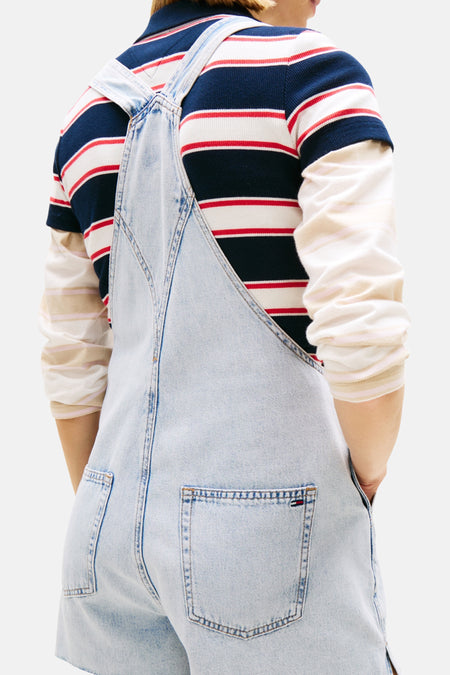 Lichtblauwe denim jumpsuit van TOMMY JEANS, rugzijde met bretels over een gestreept T-shirt.