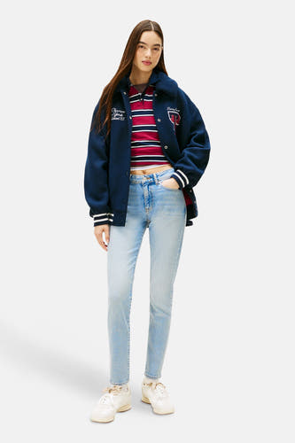 Slim fit jeans van lichtblauw denim van Tommy Jeans, gedragen met een gestreepte top en een varsity jack.
