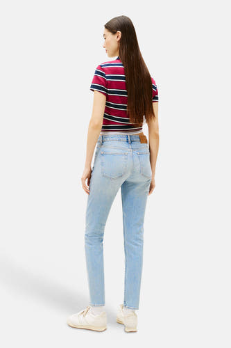 Slim jeans van lichtblauw denim van TOMMY JEANS, met een crop top met strepen en witte sneakers.
