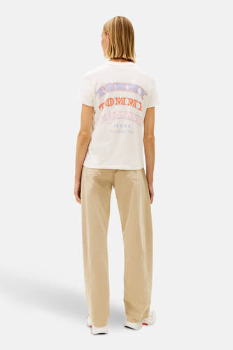 Ecru T-shirt met korte mouwen van TOMMY JEANS, met kleurrijke print op de rug, gecombineerd met beige broek en witte sneakers.
