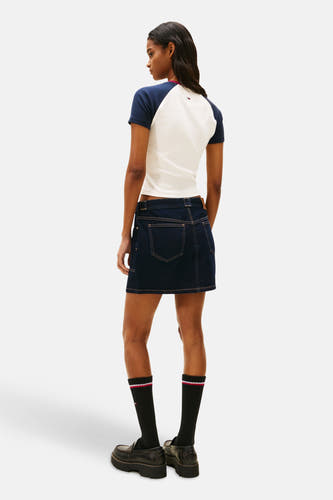 Multikleurig T-shirt met korte mouwen van Tommy Jeans, met marineblauwe mouwen, gedragen met een spijkerrok.
