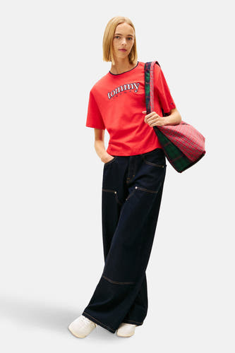Rood T-shirt met korte mouwen van TOMMY JEANS, met opschrift en gedragen met wijde jeans en een schoudertas met ruitpatroon.
