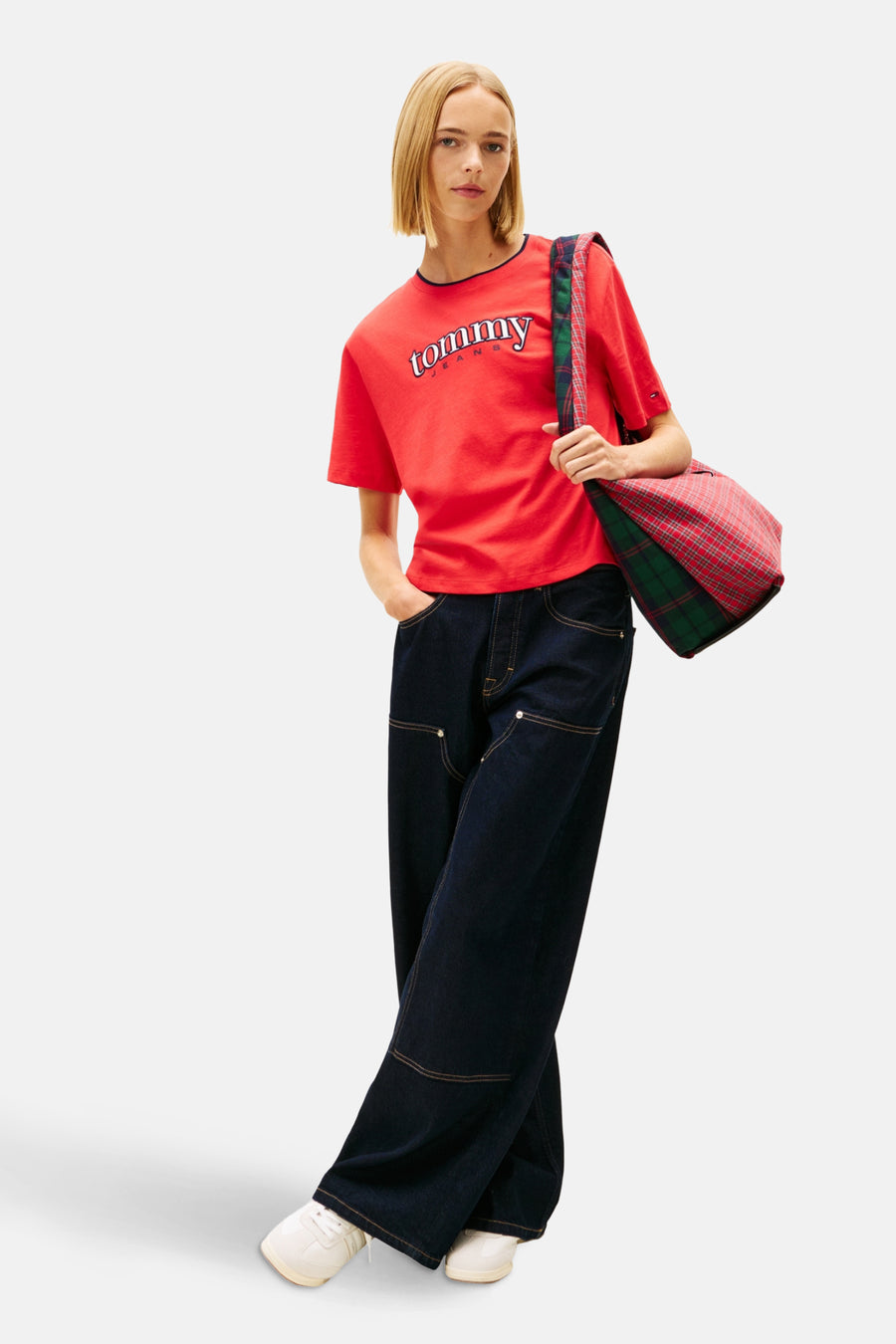 Rood T-shirt met korte mouwen van TOMMY JEANS, met opschrift en gedragen met wijde jeans en een schoudertas met ruitpatroon.