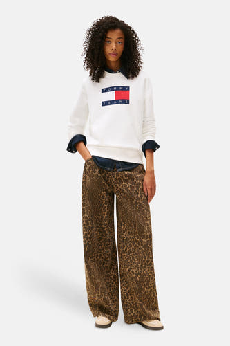 Pull-over blanc de TOMMY JEANS, avec logo sur la poitrine, porté avec un chemisier en denim et une pantalon à imprimé animal.