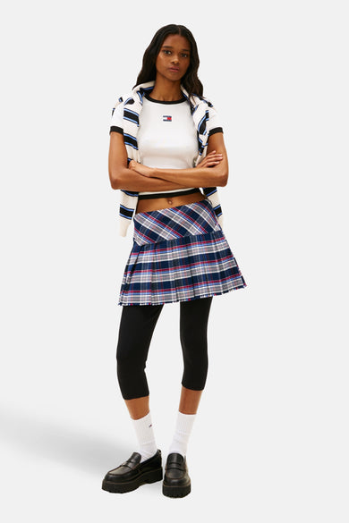 Wit T-shirt met korte mouwen van TOMMY JEANS, met een geribbelde textuur en een logo, gecombineerd met een geruite minirok en zwarte leggings.
