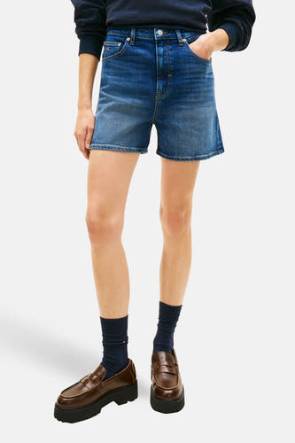 Donkere blauwe denim short van TOMMY JEANS, met bruine loafers en donkerblauwe sokken, op een witte achtergrond.
