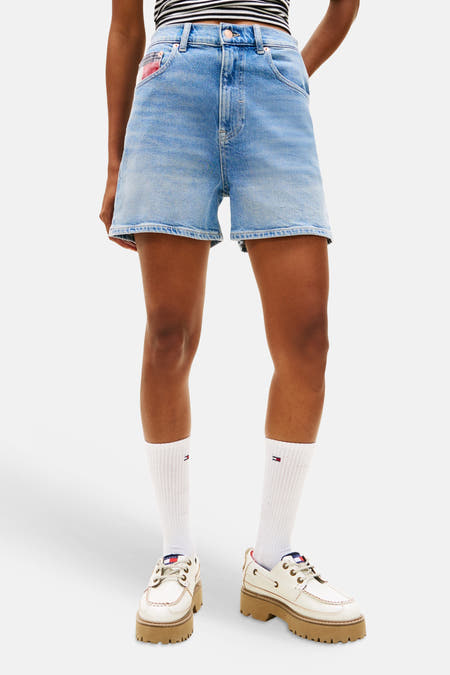 Short en jean bleu de TOMMY JEANS, avec détail de cordon de serrage et porté avec une chemise rayée et des chaussettes blanches.