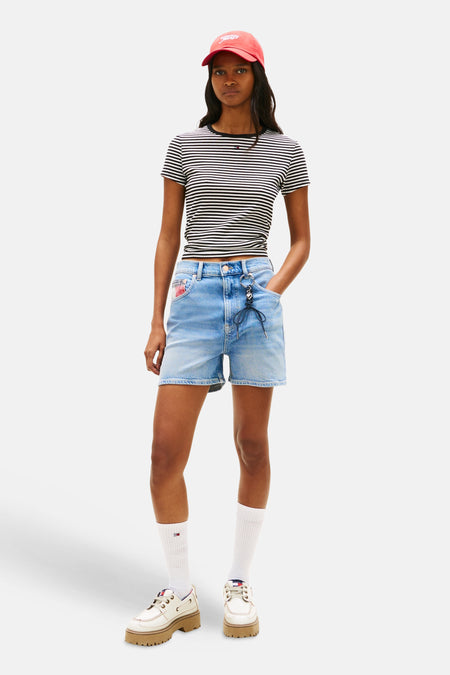 Blauwe denim short van TOMMY JEANS, met trekkoord detail en gedragen met een gestreept shirt en witte sokken.
