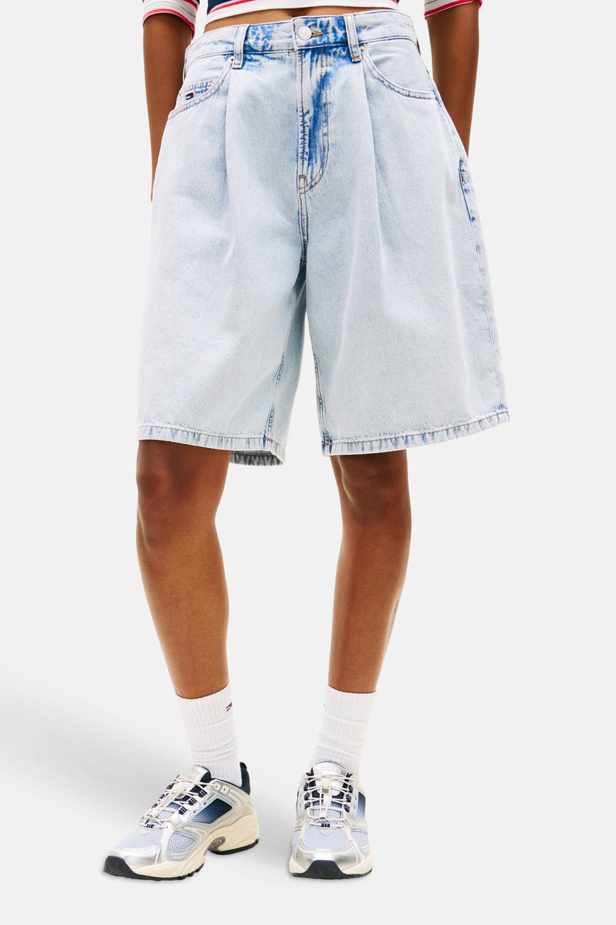 Lichtblauwe denim short van TOMMY JEANS, geplooid en wijdvallend, gedragen met witte sokken en metallic sneakers.