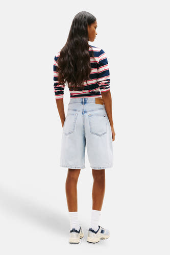 Lichtblauwe denim short van TOMMY JEANS, in de rug gezien, gecombineerd met een gestreept shirt en sneakers.