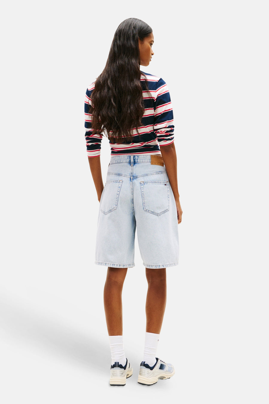 Lichtblauwe denim short van TOMMY JEANS, in de rug gezien, gecombineerd met een gestreept shirt en sneakers.