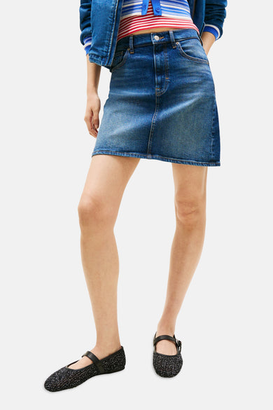Jupe courte en jean bleu foncé de TOMMY JEANS, associée à une ceinture marron, un haut rayé et une veste en jean.